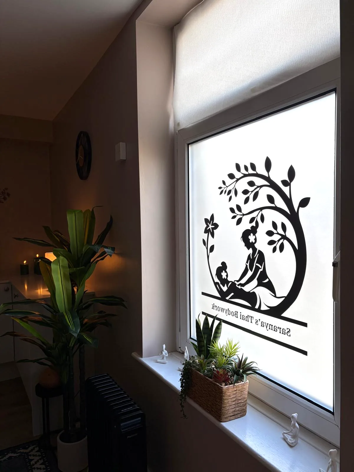 Saranya's Thai Bodywork logo on the frosted studio window beside indoor plants